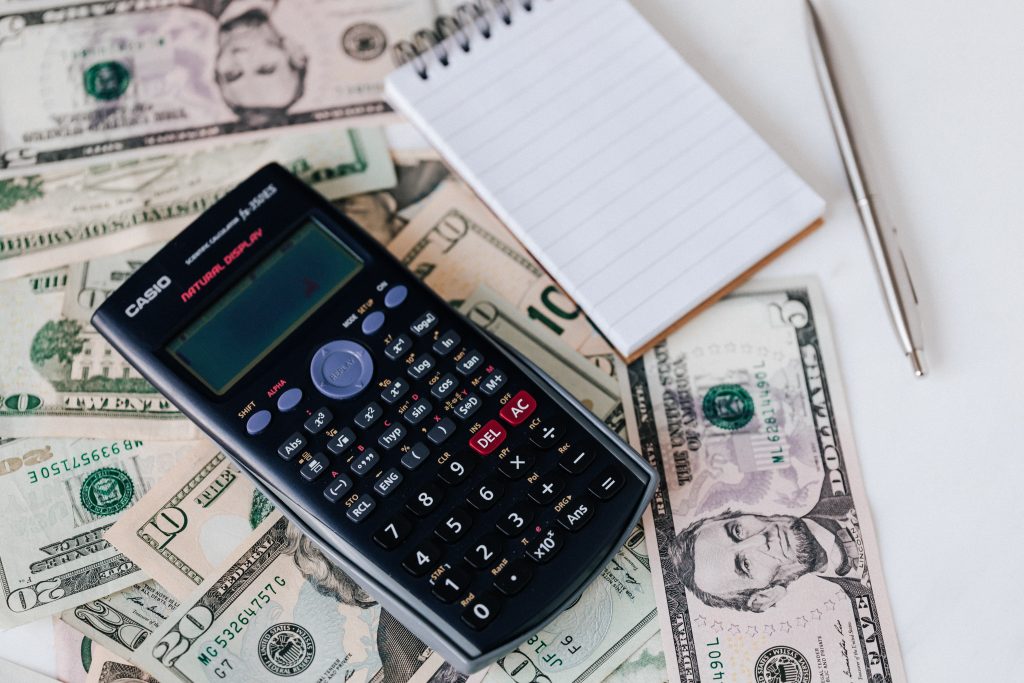 calculator and notepad placed on USA dollars stack